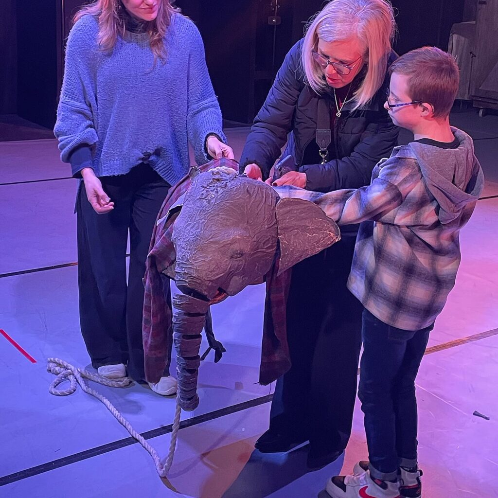 A young boy with glasses and his grandmother interact with Janu the elephant puppet.